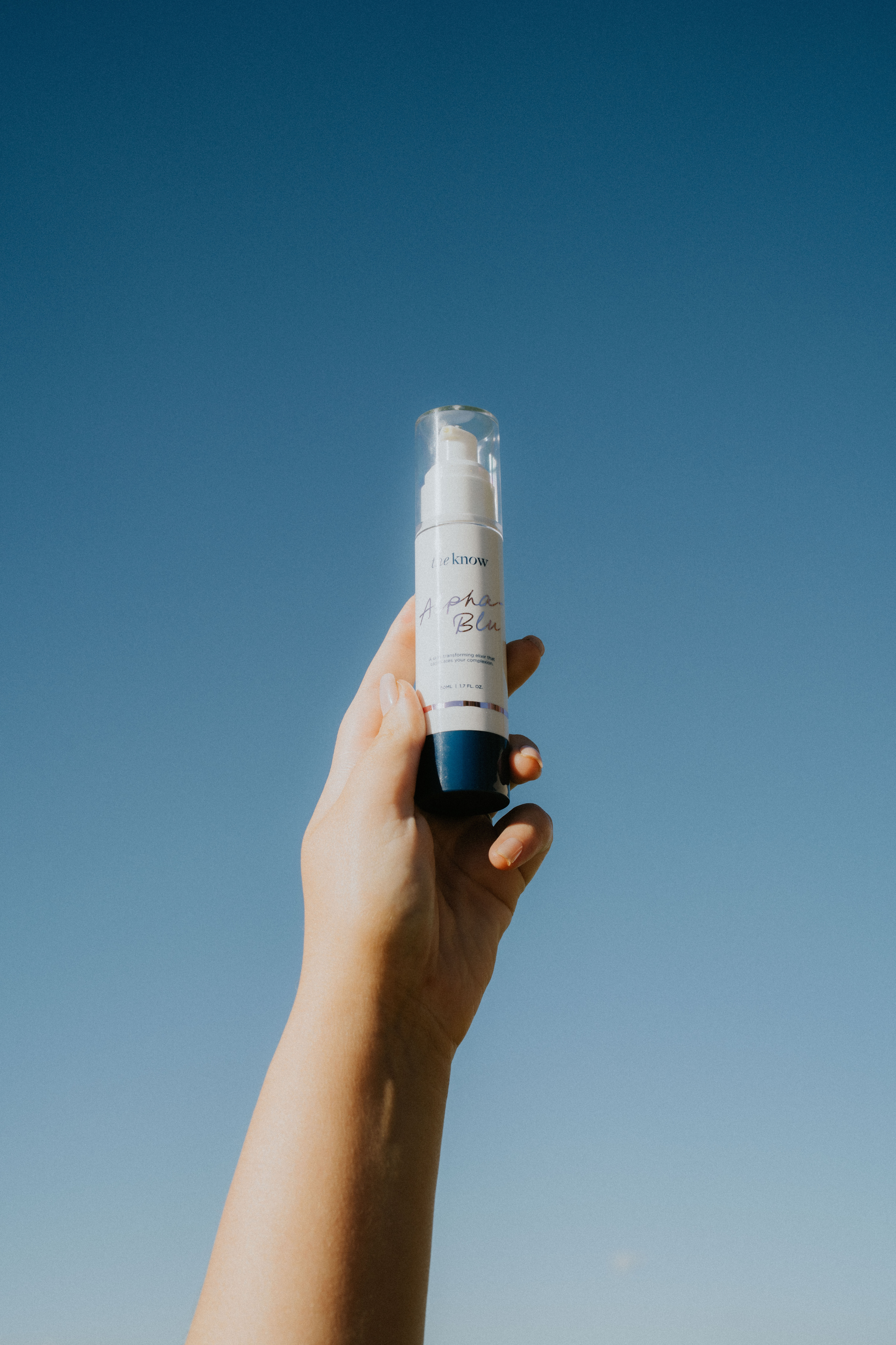 Hand holding a skincare bottle against a clear blue sky